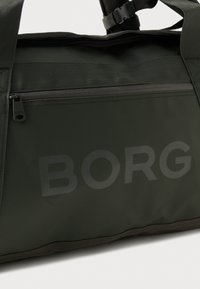 Bolsa de lona verde oscura con un bolsillo con cremallera, acabado mate, gran logo "BORG", asas reforzadas y correa de hombro ajustable.