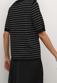 Sort stribet sweater med hvide striber, kortærmede og afslappet pasform; tekstureret strikstof; med en detalje af en baglomme.
