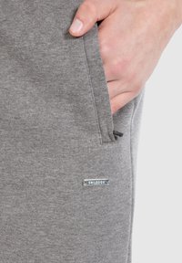 Grijze joggingsbroek met een gladde textuur, voorzien van een zijzak en een metalen logo-label op het been.