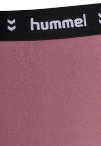 Roze sportstof met een zwarte elastische tailleband, voorzien van witte "hummel" branding en logo, gladde textuur en een rekbare pasvorm.