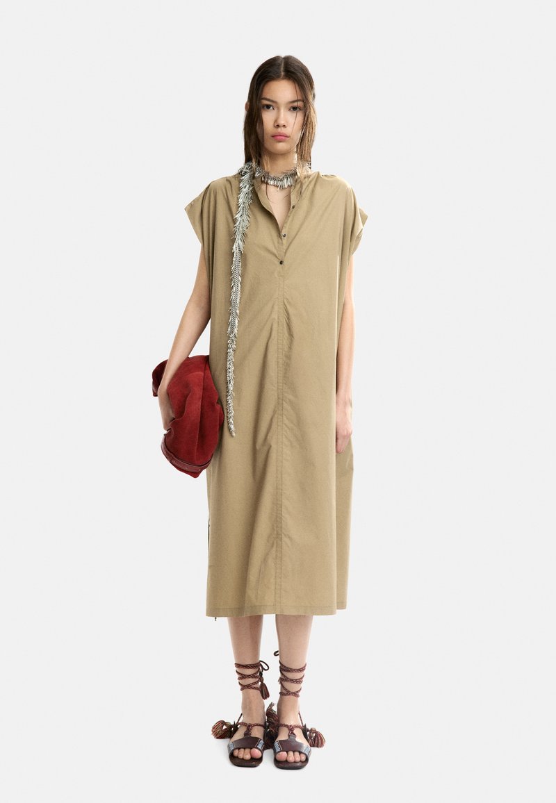 Beige kjole med korte ærmer, frontknapper, sidelommer og lige snit. Stylet med en rød suedetask og brune remsandaler.