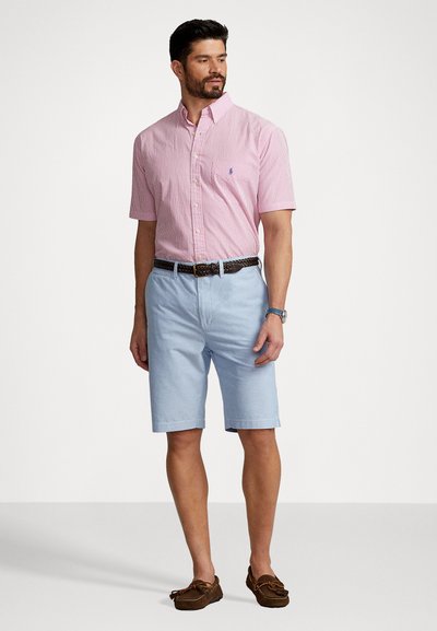 Sarkans un balts svītrots īsām piedurknēm, gaiši zili šorti, brūns teksturēts jostas, brūnas laivu kurpes. Vienkāršs, ikdienišķs vasaras apģērbs.