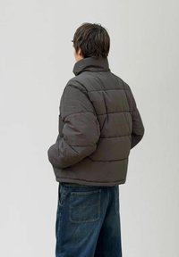 Czarna szara kurtka puchowa z wysokim kołnierzem, pikowanym wzorem i luźnym krojem. Połączona z niebieskimi dżinsami z dwoma tylnymi kieszeniami.