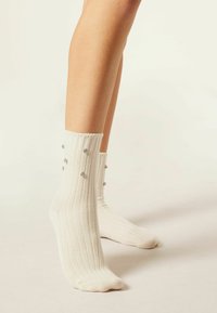 Chaussettes blanches côtelées avec des clous décoratifs argentés le long du bord supérieur. Texture douce, design à la cheville.