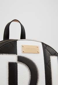 Black and white faux leather backpack featuring quilted texture, a gold logo plate, and contrasting stitching details.
