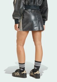 Černá sukně z umělé krokodýlí kůže se třemi vertikálními bílými pruhy. Kombinována s černými teniskami a černými ponožkami s pruhy.