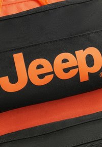 Borsa nera con accenti arancioni, dotata di un prominente logo "Jeep" arancione. La texture è robusta, adatta per l'uso all'aperto.