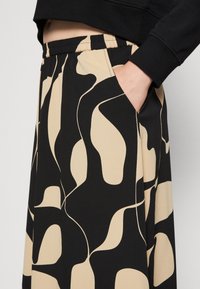 Saia padrão em preto e bege com um design fluido, cintura elástica e bolsos laterais, confeccionada em tecido leve e suave.