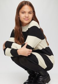 Gebreide trui met zwarte en crèmekleurige horizontale strepen, ronde hals, geribbelde textuur, gecombineerd met zwarte panty’s en enkellaarsjes.