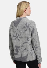 Grauer Pullover mit einem strukturierten floralem Muster in dunklerem Grau. Verfügt über einen runden Halsausschnitt und lange Ärmel, mit einer lockeren Passform.