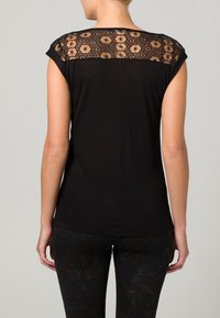 Musta lyhythihainen paita, jossa on pitsinen selkä ja kukkakuosi. Sujuva kangas, muotoiltu malli, yhdistettynä teksturoituihin mustiin legginsseihin.