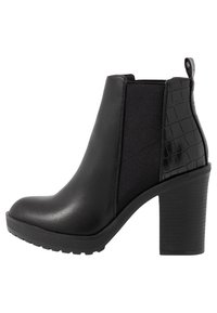 Botas negras hasta el tobillo con un tacón grueso, hechas de cuero suave y con un panel con diseño de cocodrilo y gomas elásticas en los laterales para facilitar su uso.