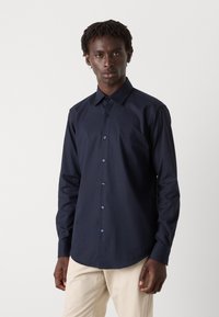 Camisa de botones azul marino hecha de una tela suave con cuello puntiagudo y mangas largas, con botones en contraste y un corte ajustado.