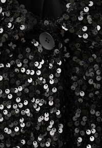 Indumento nero decorato con paillettes nere e argento lucido, con un bottone nero rotondo, che mette in evidenza una superficie testurizzata e dettagli riflettenti.