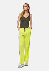 Olive green tank top and bright yellow sweatpants with a drawstring waist. Pants feature side zip accents and a textured fabric design.