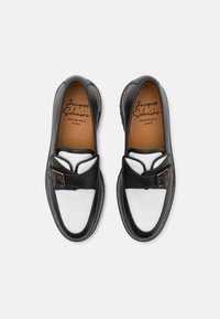 Chaussures en cuir noir et blanc avec une finition texturée, dotées d'une boucle décorative et de coutures contrastées sur un design à bout rond.