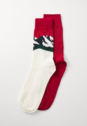 Red and white socks; one features a mountain design with green accents, the other is solid red with white polka dots. Knitted texture.