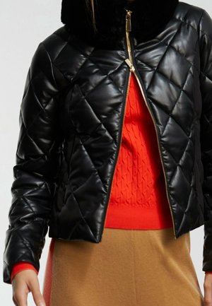 Svart quiltad jacka med glansig finish och en mjuk svart krage, med en guldfärgad dragkedja och en orange texturerad tröja under.
