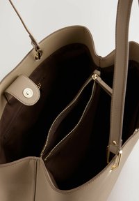 Beige Leder-Handtasche mit strukturiertem Finish. Sie verfügt über einen goldfarbenen Druckverschluss und eine innere Reißverschlusstasche. Gefüttert mit braunem Stoff.