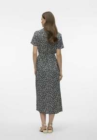 Robe midi noire à fleurs avec manches courtes, ceinture à la taille et ourlet complet. Présente des motifs floraux blancs. Portée avec des sandales beiges à lanières.