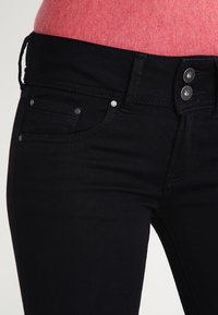 Jeans de denim negro con un diseño ajustado, dos bolsillos frontales y cierre de doble botón, con una textura suave y detalles de costura sutiles.