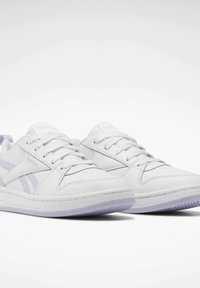 Vitaidrottsskor i vitt med lila accenter, tillverkade av läder. Har en vadderad sula, snörningsdesign och ett distinkt sidosymbol.