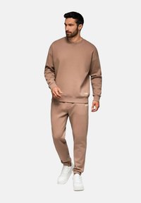 Beige sweatshirt och byxor i mjukt material, med ribbad mudd och avslappnad passform. Bärs med vita sneakers. Litet logotyp på materialet.