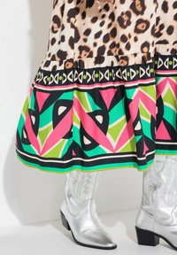 Leopardmønstret top med en flared, flerfarvet geometrisk mønstret nederdel. Udstyret med sorte, pink, grønne og sølv cowboystøvler.