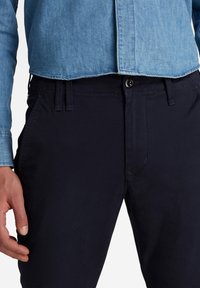 Marinblå bomullsshorts med rak skärning, slät framtill och bälteshällor, parat med en ljusblå denimskjorta med knäppning.