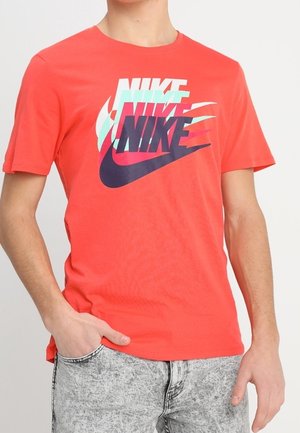 Rød bomulds t-shirt med lagdelte Nike-logoer i blå og grøn. Kortærmet og med rund hals, parret med grå mønstrede jeans.