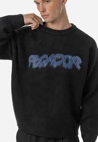 Sweater preto de malha com uma impressão gráfica azul felpuda apresentando a palavra "PLUR" na parte da frente. Possui um decote redondo e um corte descontraído.