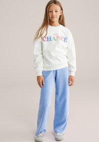 Gaiši zaļa kokvilnas krekla ar daudzkrāsainu "TAKE A CHANCE" tekstu, apvienota ar ziliem ribotiem platām biksēm, lai radītu ikdienišķu izskatu.