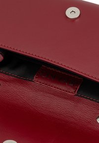 Borsa a tracolla rossa in pelle con una texture liscia, chiusura a scatto in metallo argentato e foderatura interna nera con etichetta.