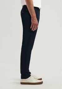 Marineblauwe slim-fit broek met een gladde textuur, voorzien van zijzakken en een knoopsluiting, gedragen met witte sneakers.