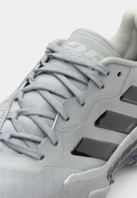 Grauer Sportschuh aus strukturiertem Material, mit schwarzen Akzenten und einem stromlinienförmigen Design. Die Schnürsenkel sind grau und haben eine ausgeprägte Textur.