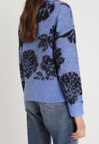 Modrý pletený svetr s květinovým vzorem v tmavě modré barvě. Měkká textura s volným střihem a žebrovanými manžetami, navržený pro volnočasové nošení.