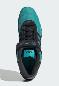 Teal og sort sneaker med quiltet struktur, sorte snørebånd og en polstret krave. Har logo detaljer og tre sorte striber på siden.
