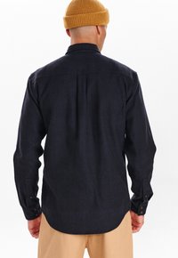 Granatowa koszula z długim rękawem o zaokrąglonym dole, luźny krój oraz mankiety zapinane na guziki. Posiada tylną yoke oraz teksturowany materiał.