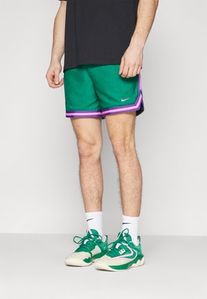 Pantalones cortos deportivos verdes con rayas moradas, hechos de una tela texturizada. Combinados con zapatillas verdes y calcetines blancos. Camiseta negra sencilla.