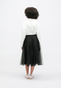 Biela košeľa na gombíky, čierna tylová sukňa s vrstvenou textúrou a svetlé šnurovacie topánky. Jednoduchý dizajn s kontrastom.