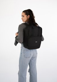 Sac à dos noir avec plusieurs compartiments, tissu robuste, forme rectangulaire, bretelles rembourrées et poche zippée à l'avant. Porté sur le dos.