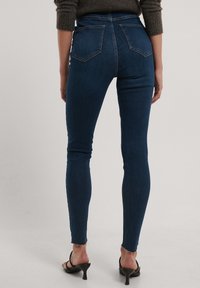 Tmavě modré skinny džíny s vysokým pasem, hladkým povrchem a surovým lemem. Předností jsou dvě zadní kapsy a těsný střih po celé délce nohavic.