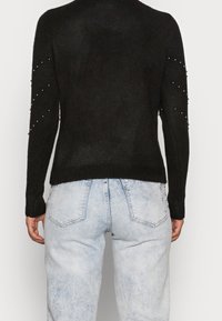 Czarny sweter z dzianiny o fakturowanym wykończeniu, z koralikowymi detalami na rękawach, w połączeniu z jasnoniebieskimi spodniami o wysokim stanie.