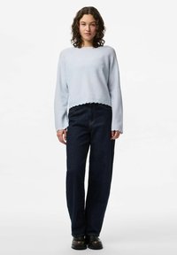 Ljusblå kort tröja med vågig nederkant, i kombination med högmidjade mörkblå vida jeans och svarta kraftiga skor.