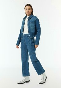 Jeansowa kurtka i pasujące spodnie z wysokim stanem w średnim niebieskim odcieniu. Kurtka posiada dwie przednie kieszenie oraz skrócony fason. Srebrne botki do kostki.