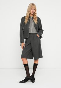 Giacca cropped in pelle grigia, maglione a coste, pantaloni corti grigi con texture, calze nere fino al ginocchio e stivaletti neri con tacco.