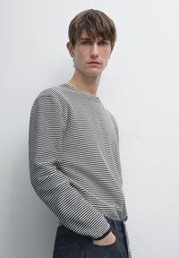 Svart- och vitrandig långärmad topp med rund halsringning, bärs med mörk denim. Har ribbade mudd och en avslappnad passform.