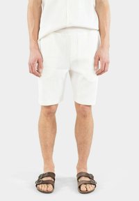 Vita kordshorts med en slät textur, som har en rak framsida och sidofickor. Bärs med bruna sandaler som visar en minimalistisk design.