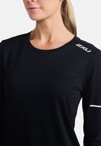 Maglia atletica nera a maniche lunghe realizzata in tessuto texturizzato, con logo bianco sulla spalla e un design minimalista con scollatura rotonda.
