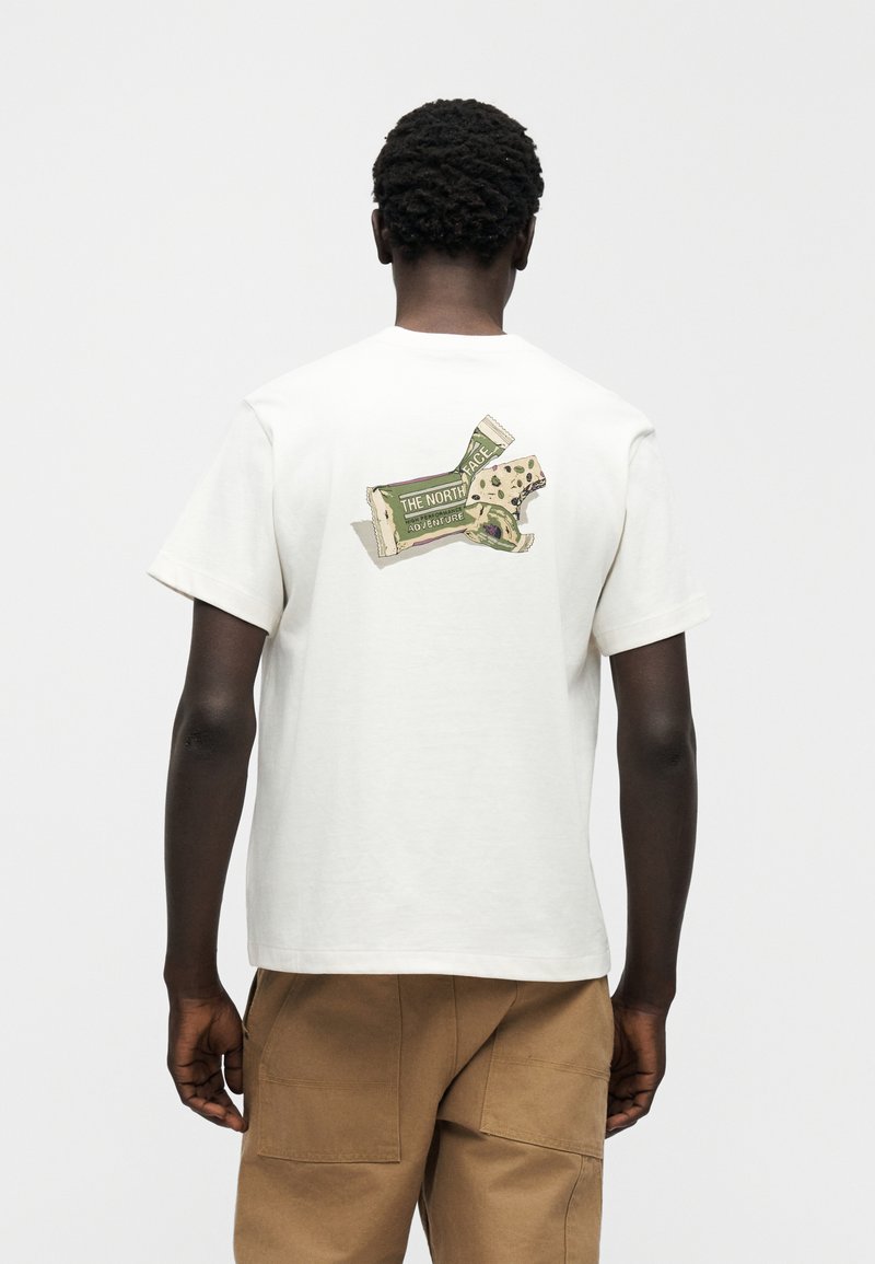T-shirt en coton blanc à manches courtes, avec un motif de barre snack au dos. Coupe décontractée avec un col rond.